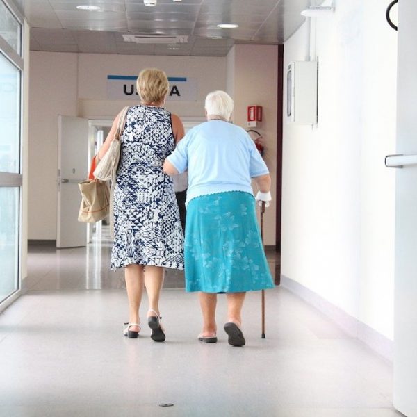 An elderly patient with her carer walking down a hospital corridor.