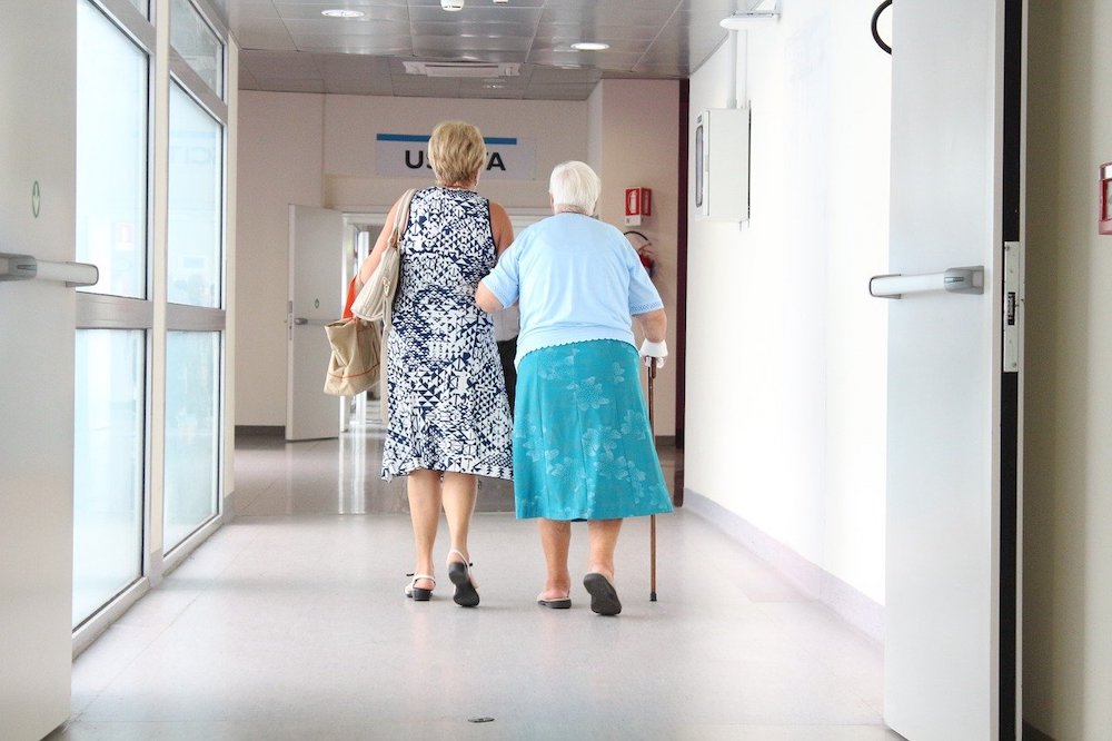 An elderly patient with her carer walking down a hospital corridor.