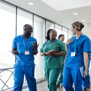 A diverse group of healthcare professionals in medical scrubs walk together through a bright hospital corridor.